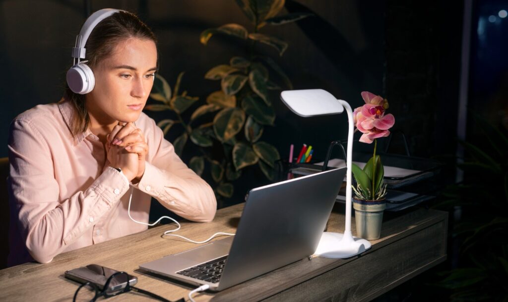 Medium shot woman working late at night with a Desk Lamp and laptop