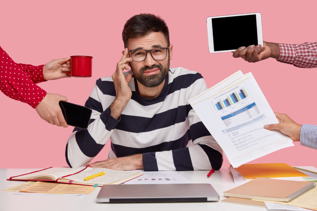 Home Tech Productivity - Brunet man sitting at desk surrounded with gadgets and papers
