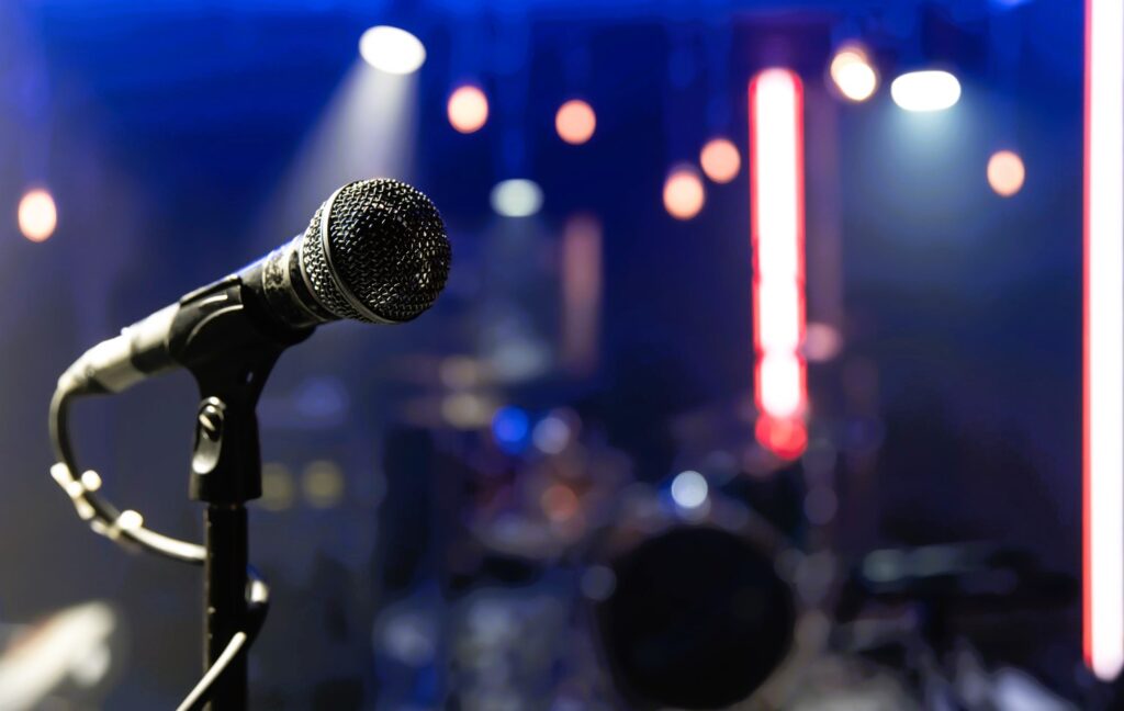 A close-up of a silver microphone on a stand, ready for a karaoke performance in a dimly lit room with blue stage lights