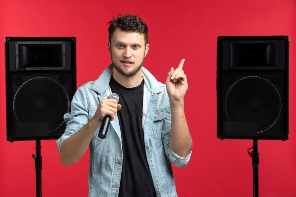 A person singing into a microphone in front of a karaoke system with a large speaker