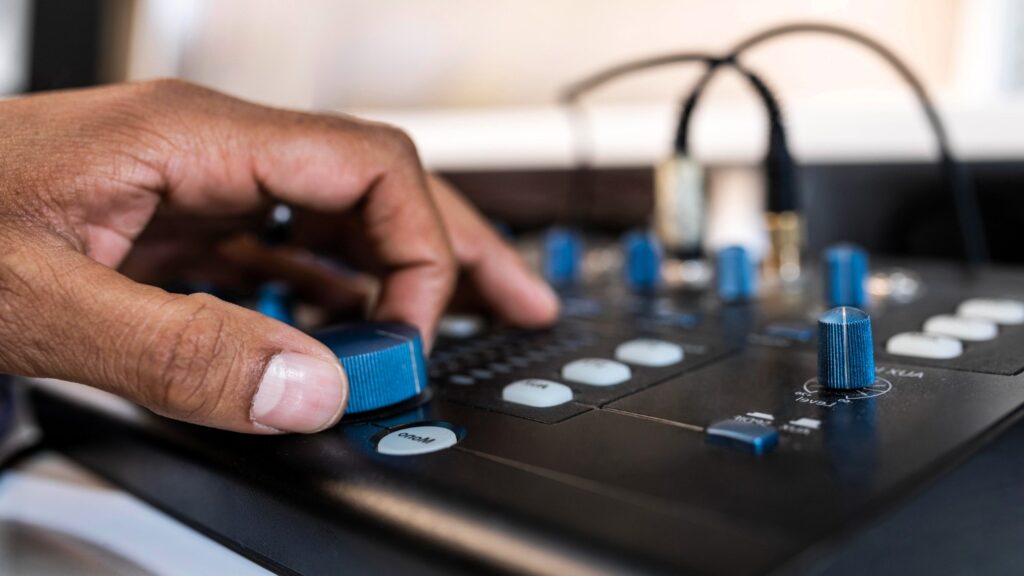 A hand adjusting the volume knob on a black audio mixer, ensuring optimal sound levels for a home karaoke setup